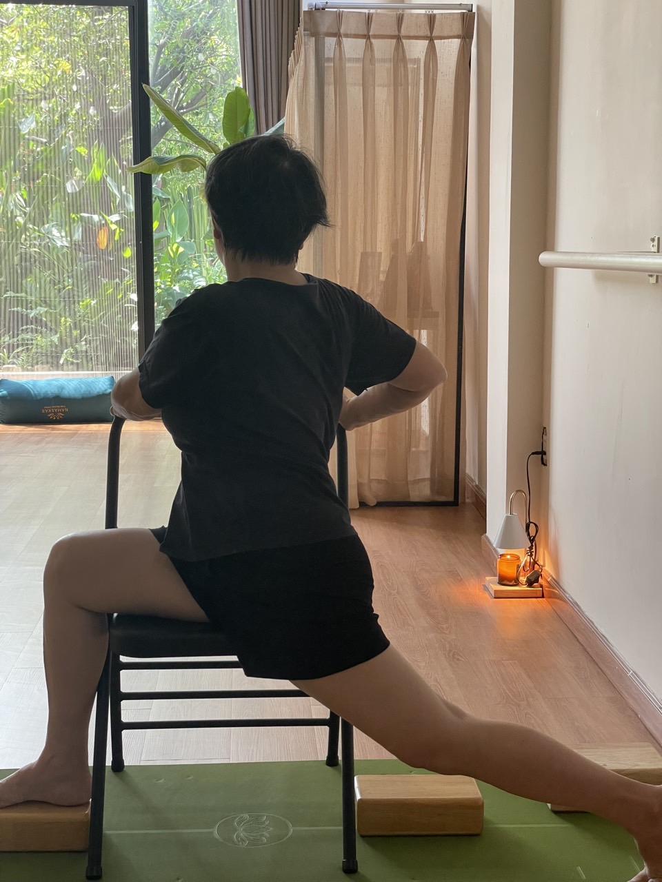 Học viên cao tuổi tập tư thế Chiến binh có ghế tựa làm điểm bám — rèn phản xạ thăng bằng chủ động